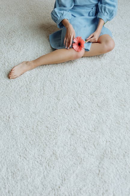 Close-up of a beige carpet with a decorative floral pattern in brown and darker shades, showcasing a section with a slightly different texture and color intensity. The carpet appears clean and well-ma